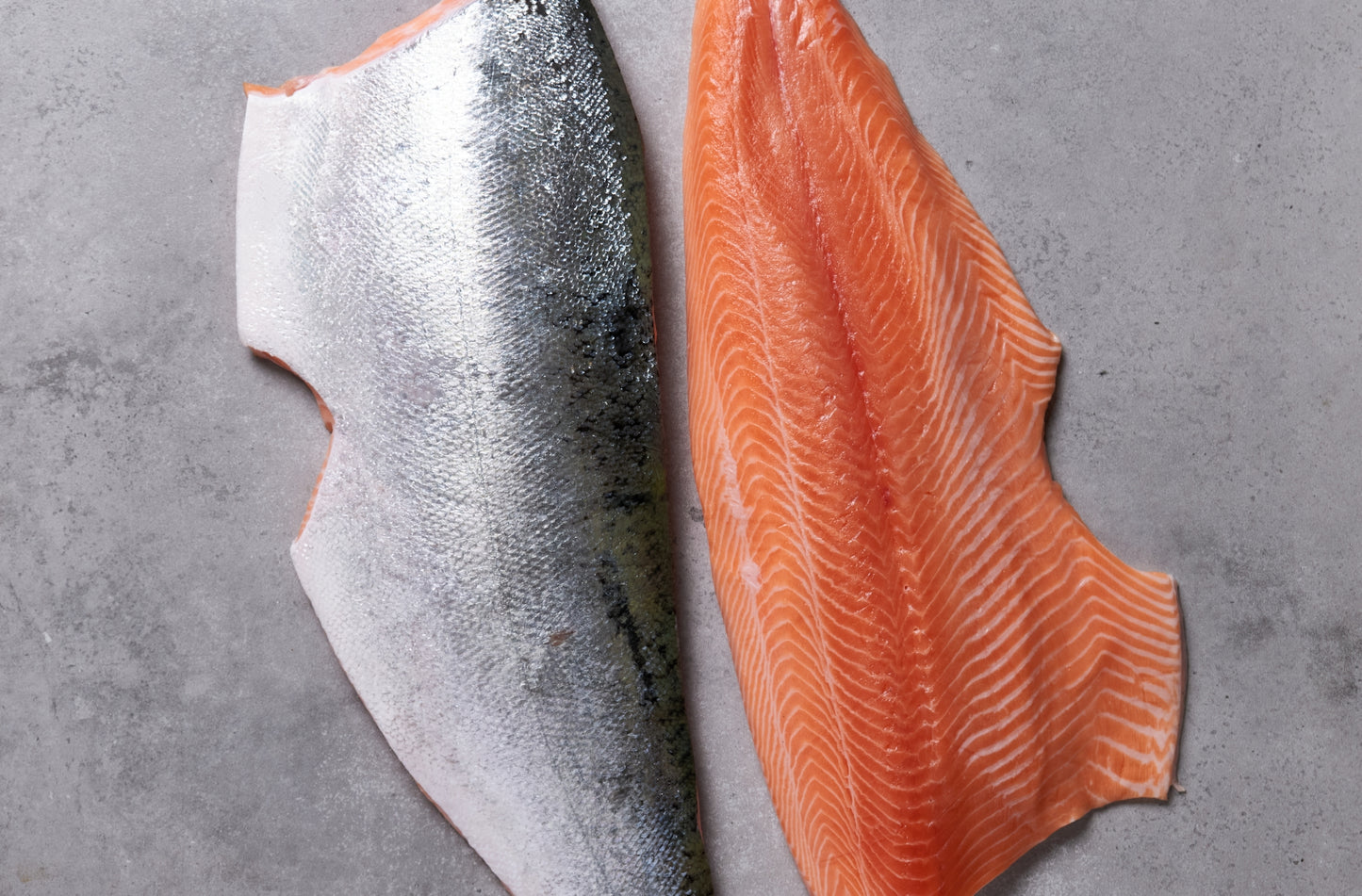 Two fresh salmon fillets, one fillet skin side up.
